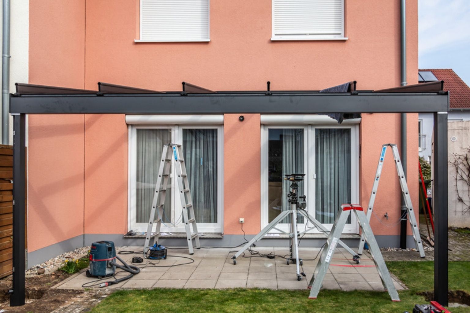 Ny overdækning i sort aluminium monteres mod facaden på et rækkehus, med stiger og værktøj på terrassen