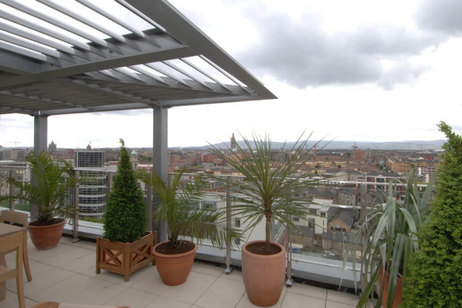 Tagterrasse med pergola og planter i krukker med udsigt over en by