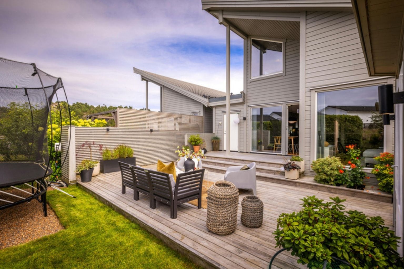 Træterrasse med sofa, stole og potteplanter ved et moderne hus og en græsplæne