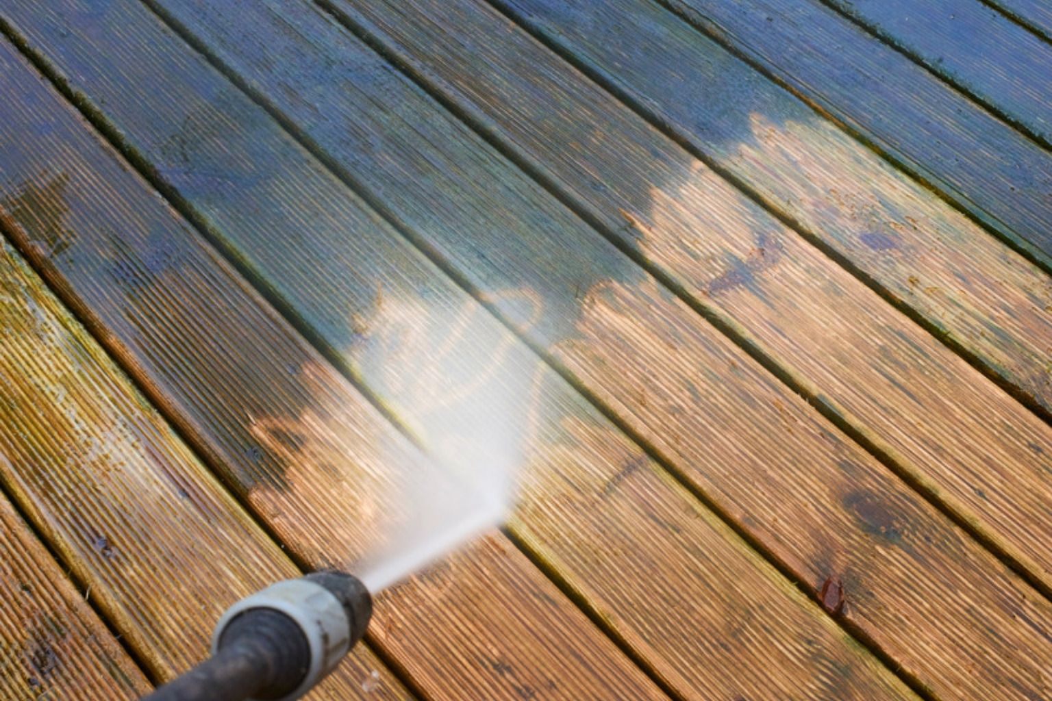 Vandstråle fra en højtryksrenser rammer rillede terrassebrædder med alger og snavs